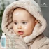Baby mit aufgetragener natürlicher Babycreme im Gesicht in warmer Felljacke – sanfte Pflege für empfindliche Haut